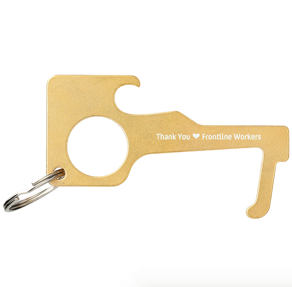 A brass coloured no touch keychain tool that lets you open doors without touching them to be more safe during the pandemic.