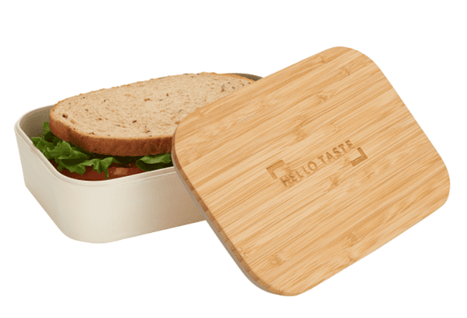 A lunch box with a sandwich inside and a bamboo lid next to it.