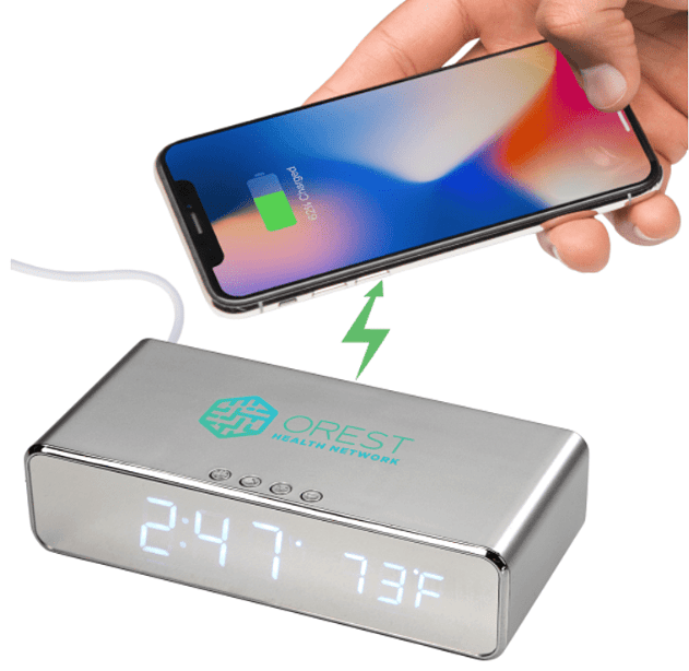 A hand holding a phone over a silver desk clock.